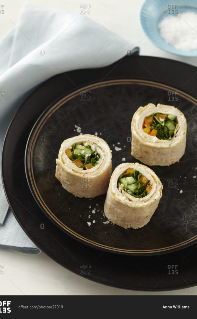 Three rolls of food on a black plate.