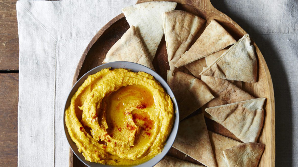 A bowl of hummus next to some pita bread.